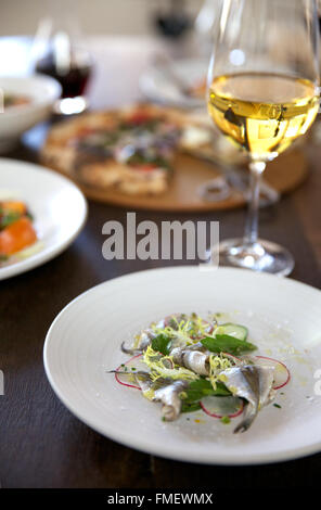 Una piastra di crudo di sardine preparate con ravanelli & green e un bicchiere di vino bianco e le altre piastre di cibo che circonda. Foto Stock