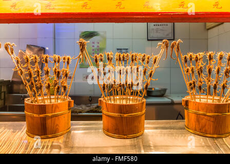 Scorpioni e altri insetti su spiedi vengono offerti da un venditore in bancarelle del mercato di Wangfujing Snack Street Foto Stock