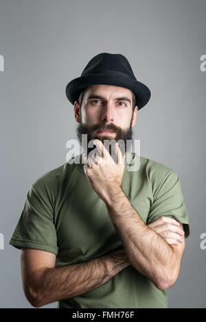 Vista frontale di pensosa uomo accarezzare la sua barba guardando la fotocamera. Headshot ritratto su studio grigio Sfondo con vignette. Foto Stock