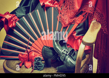 Abbigliamento per la danza flamenca. Nero scarpe, ventilatore, sciarpa rossa con fiocchi di carta e le rose sono giacenti su un vintage sedia in legno. Foto Stock