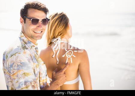 Uomo che fa un simbolo del sole sul retro womans durante la applicazione di una crema di protezione solare Foto Stock