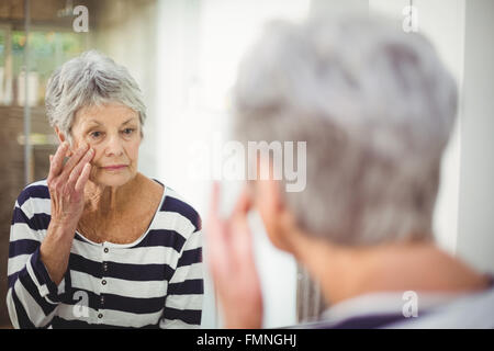 La riflessione di senior donna che guarda la pelle a specchio Foto Stock