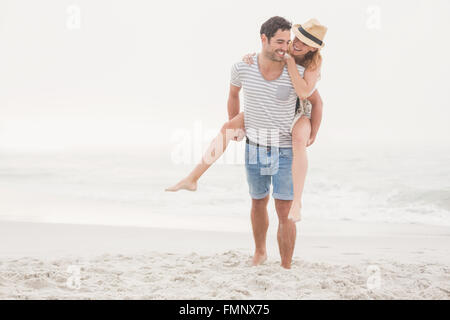 L uomo dando una piggy back per donna sulla spiaggia Foto Stock