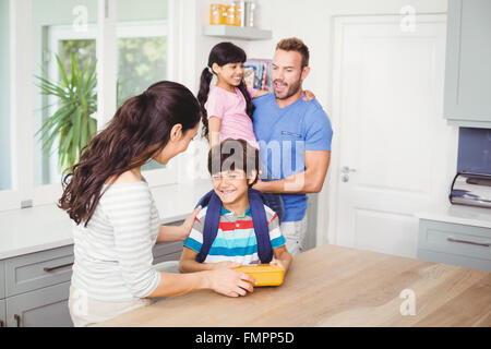 Madre dando scatola di pranzo al figlio col padre daughte portante Foto Stock