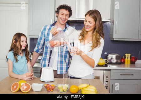 Sorridente madre versando il succo di frutta in vetro con la famiglia Foto Stock