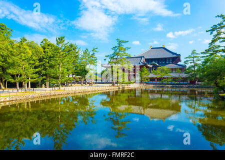 Percorso pedonale e tranquillo lago riflette il rosso anteriore porta d ingresso al Daibutsuden visto in distanza sulla splendida e soleggiata blu Foto Stock