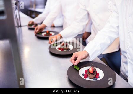 Team di chef la finitura piatti da dessert in cucina Foto Stock