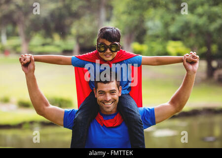 Ragazzo in costume da supereroe seduto sulla spalla padri Foto Stock