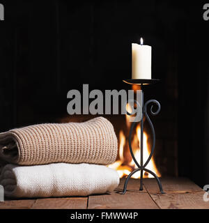 Caldo cose di lana e candela in candelabro vicino al camino sul tavolo di legno. Inverno e vacanze di Natale concetto. Foto Stock