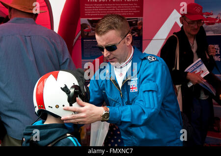 Un membro delle frecce rosse si inserisce un casco di volo su un bambino a Eastbourne Air Show Foto Stock