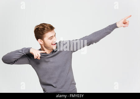 Felice bel giovane rivolto lontano con entrambe le mani su sfondo bianco Foto Stock