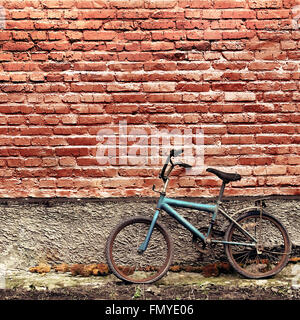 Vecchio arrugginito bicicletta vintage appoggiata contro un muro di mattoni Foto Stock