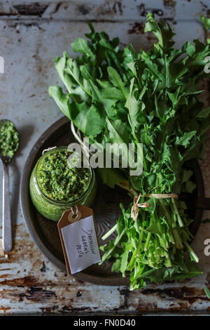 Mazzetto di fresche foglie di tarassaco e un vasetto di pesto Foto Stock