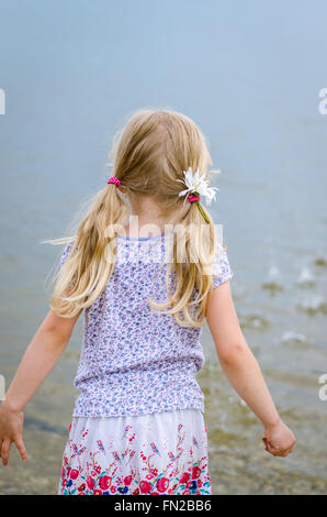 La ragazza con i capelli lunghi che lanciano pietre in acqua vista posteriore Foto Stock