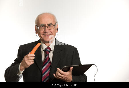 Vecchio imprenditore senior lavora con nero computer tablet, indossando il business suit, mangiando la carota Foto Stock