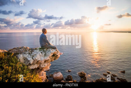 L'uomo guarda Sunrise seduto sulla roccia accanto alla scogliera. Malta, Europa Foto Stock