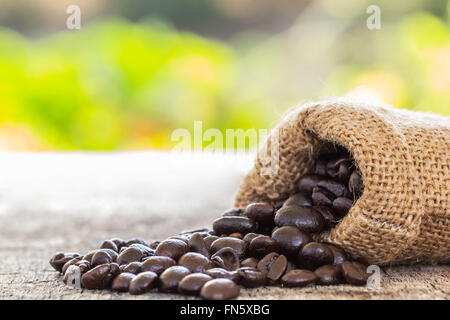 Immagine ravvicinata i chicchi di caffè versata dal sacco sul vecchio tavolo in legno verde con sfondo bokeh di fondo Foto Stock