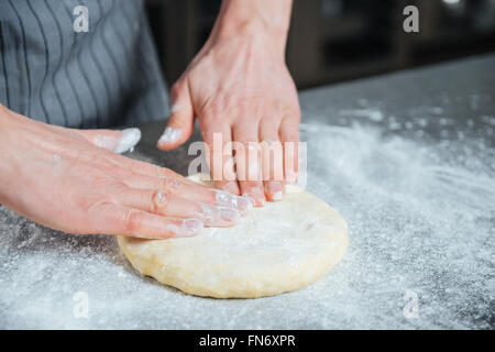 Primo piano delle mani maschio lavorazione dell'impasto sul tavolo della cucina Foto Stock