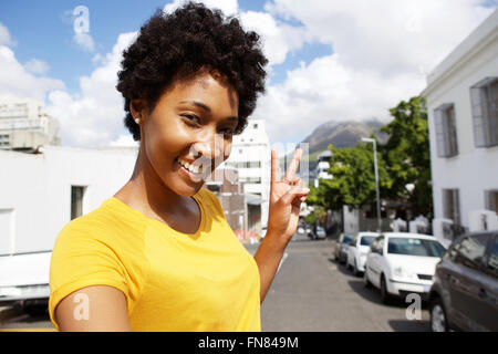 Selfie ritratto di sorridente giovane donna in piedi sulla strada di città gesti segno di pace Foto Stock