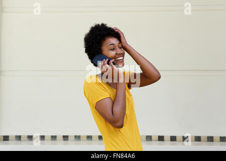 Ritratto di giovane donna nera parlando al telefono cellulare e sorridente con la sua mano sulla testa Foto Stock