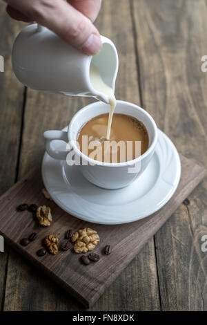 La crema che viene versato in un caffè in una tazza bianca. Foto Stock