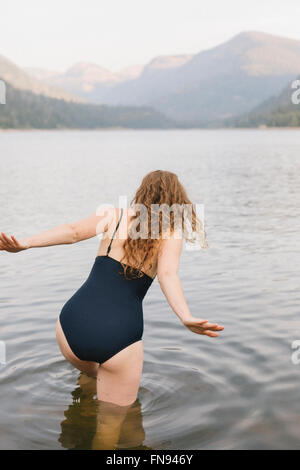 Una donna in costume nero wading in un tranquillo lago di montagna. Foto Stock