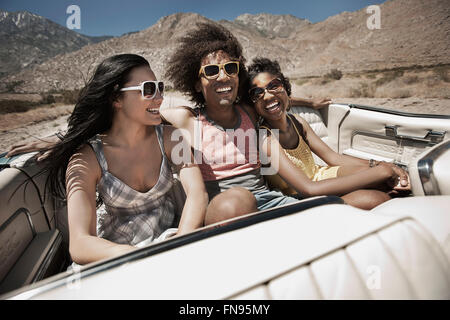 Tre giovani in un colore blu pallido autovettura convertibile, guida su strada aperta attraverso una piatta pianura a secco, Foto Stock