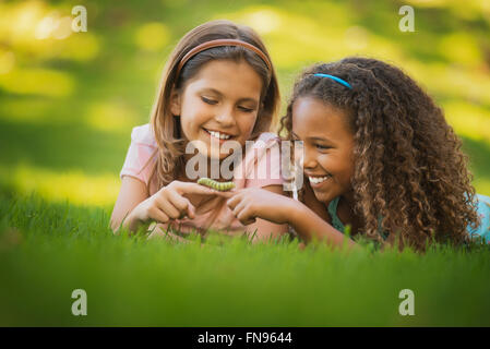 Due ragazze sdraiati sull'erba, una holding di un bruco verde sul suo dito. Foto Stock