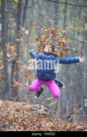 Ragazza di salto e gettando le foglie di autunno in aria Foto Stock