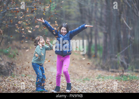 Un ragazzo e una ragazza gettando le foglie di autunno in aria Foto Stock