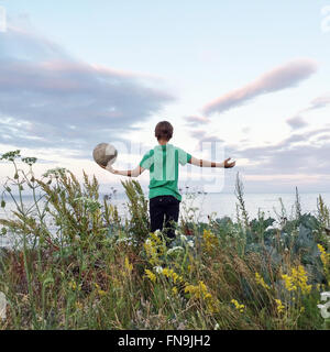 Ragazzo in piedi in un campo tenendo un calcio, Ringshaug, Tonsberg, Norvegia Foto Stock