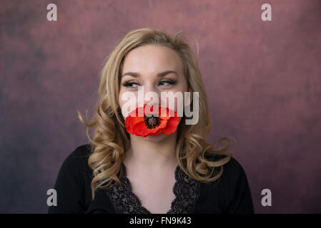 Ritratto di una ragazza con un fiore di papavero in bocca Foto Stock