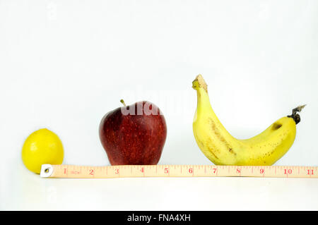 Nastro di misurazione che mostra i pollici è avvolta intorno a un limone, mela, banana su una superficie bianca, Foto Stock