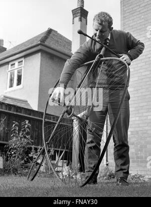 Uomo con Penny Farthing bicicletta in bisogno di riparazione con una ruota deformata 1960s Foto Stock