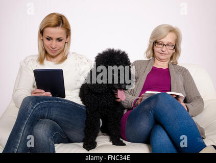 Giovane donna e sua madre seduta su un divano bianco con il loro barboncino nero. Foto Stock