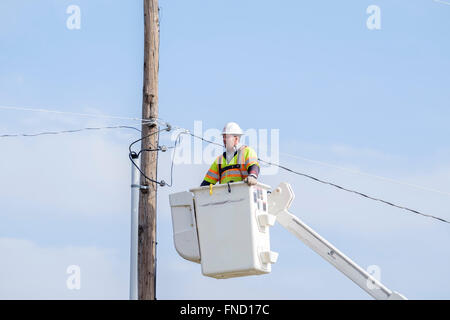 Un lineman viene abbassata al suolo in un sollevamento benna dopo la riparazione di una linea elettrica. Oklahoma City, OK, Stati Uniti d'America. Foto Stock