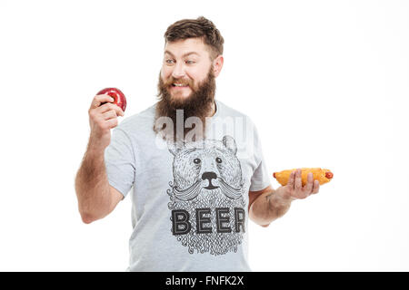 Allegro uomo bello con la barba azienda apple e hot dog e la scelta di cibo sano su sfondo bianco Foto Stock