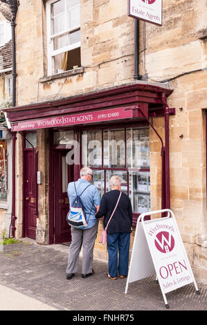 Un elderley giovane guardare in un agente immobiliare nella finestra pretty Cotswold città di Burford , Oxfordshire , Inghilterra , Inghilterra , Regno Unito Foto Stock