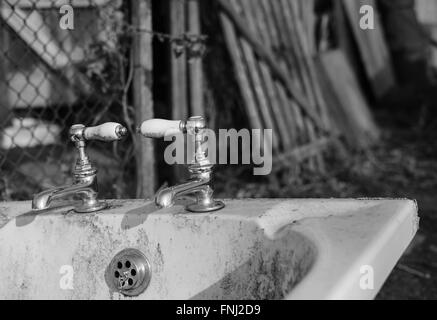 Bagno in ceramica antico abbandonato e rubinetti d'acqua cromati come visto in un campo, con il bagno utilizzato come un canale d'acqua. Foto Stock