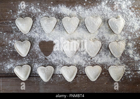 A forma di cuore ad ravioli cospargere di farina, su sfondo di legno. Ravioli di crudo cuori. Gnocchi di cottura. Vista dall'alto. Foto Stock