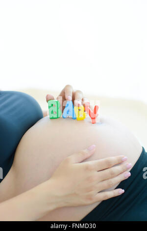 Giovane donna incinta con la lettera i blocchi baby controllo ortografico sul suo ventre in gravidanza Foto Stock