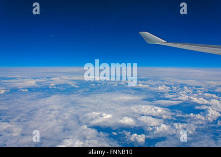 Vista da un aereo di linea finestra sopra le nuvole guardando verso il basso sulla Holland con la luna visibile in chiaro cielo blu sopra Foto Stock