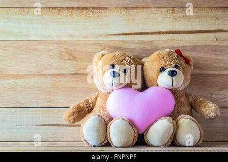 Giovane orsacchiotto con rosa a forma di cuore sul cuscino plank wood board, concetto di San Valentino Foto Stock