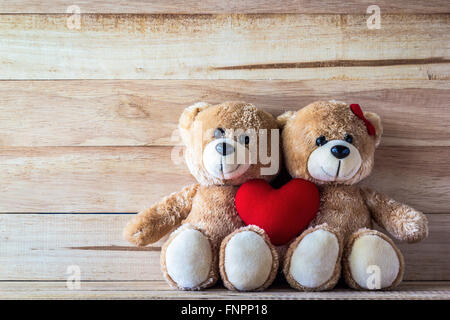 Giovane orsacchiotto con rosa a forma di cuore sul cuscino plank wood board, concetto di San Valentino Foto Stock