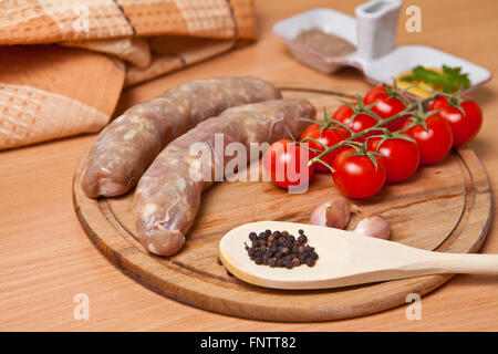 Salsicce in budello naturale su di un tagliere con pomodoro ciliegino Foto Stock