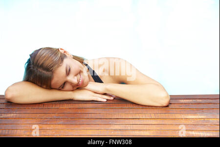 Attraente sorridente brunette donna appoggiata sul bordo della piscina Foto Stock