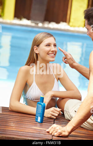 Felice coppia giovane in vacanze vicino alla piscina l'applicazione di crema solare Foto Stock