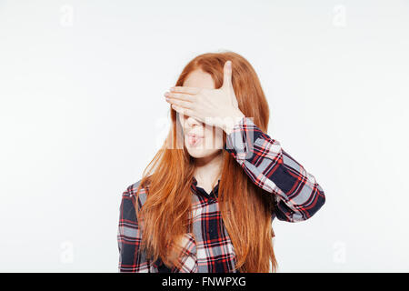 Redhead donna che copre la sua gli occhi e che mostra la linguetta isolata su uno sfondo bianco Foto Stock