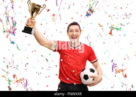 Calcio gioiosa giocatore in possesso di un trofeo di oro e di celebrare con i confetti streamers intorno a lui isolato su sfondo bianco Foto Stock