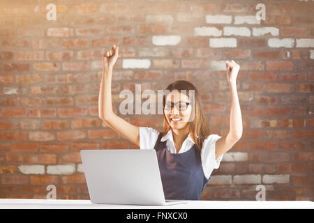 Immagine composita di felice imprenditrice utilizzando laptop e bracci di sollevamento Foto Stock